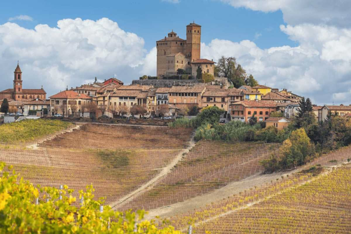 Veduta aerea di un suggestivo borgo italiano con vigneti terrazzati e cantina storica scavata nella roccia, circondato da paesaggio collinare al tramonto