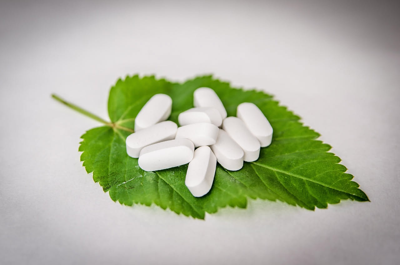Assortimento di integratori naturali in flaconi e capsule su sfondo bianco con foglie verdi di primavera