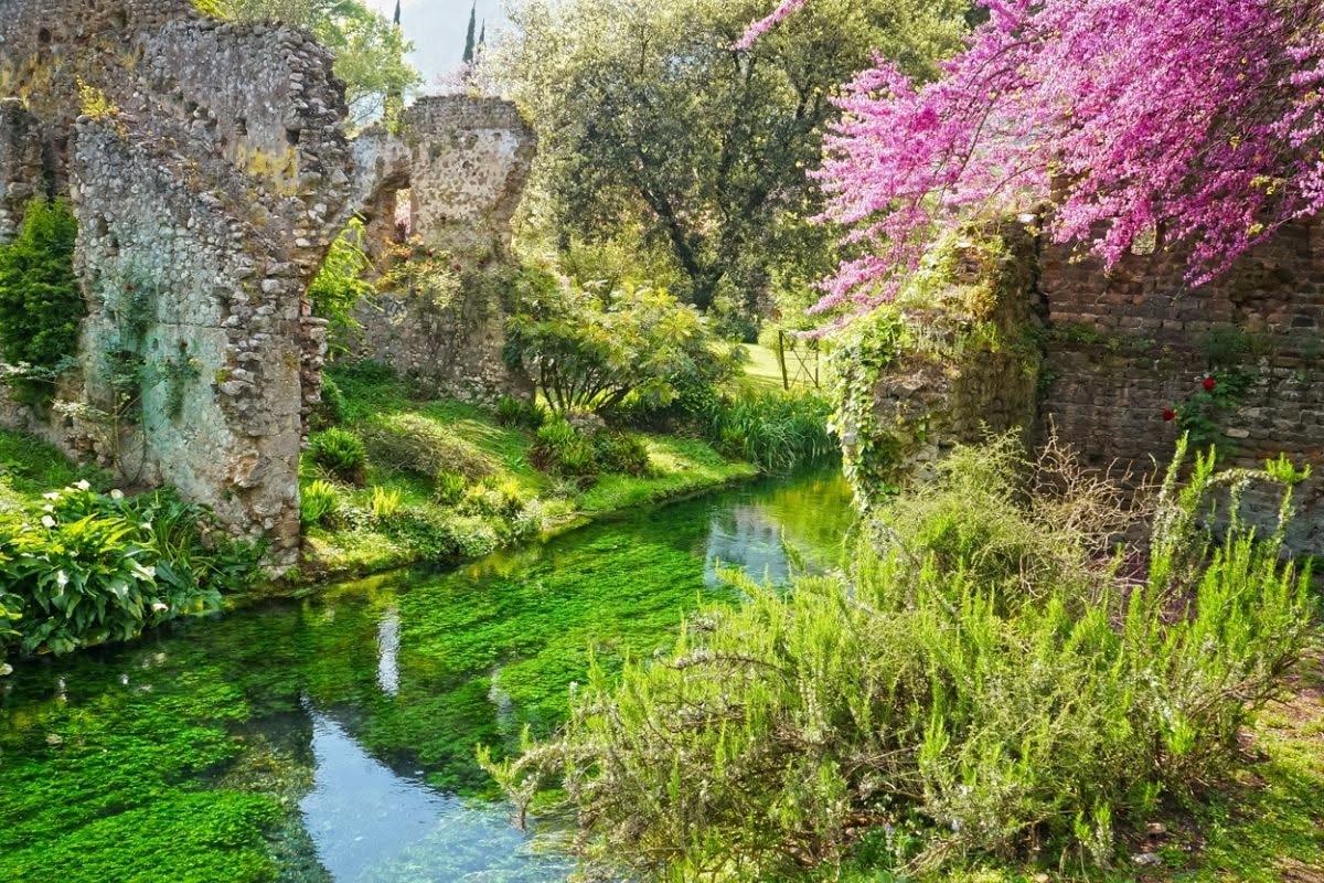 Il giardino di Ninfa con rovine medievali coperte di muschio, querce secolari e piante rare che crescono tra le pietre antiche