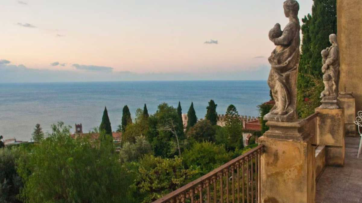 Terrazza del belvedere di Villa Cimbrone con vista sul mare, busti in marmo bianco tra piante rampicanti e balustrata in pietra, cielo azzurro sullo sfondo