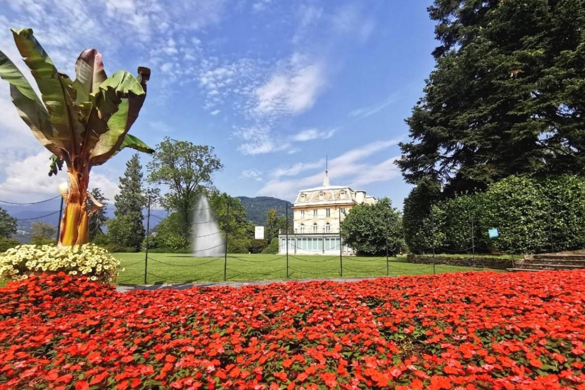 Veduta del parco della Villa Olmo a Como con prato verdeggiante, alteri d'alto fusto, la villa neoclassica sullo sfondo e il lago Como con riflessi azzurri all'orizzonte