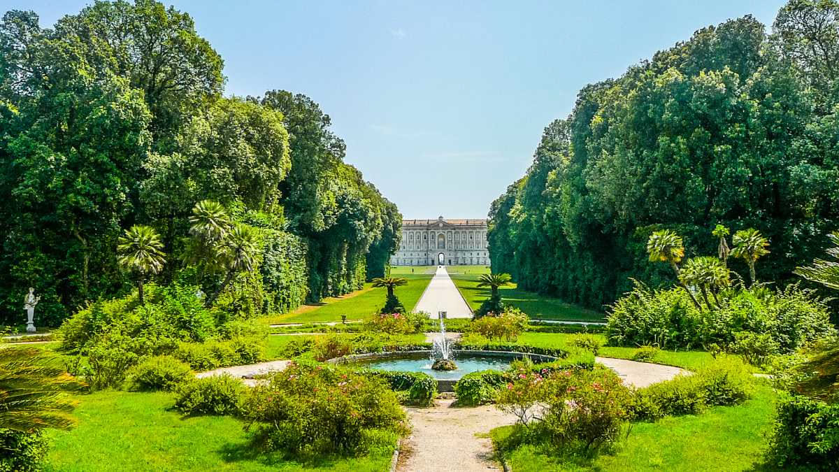 Viale centrale della Reggia di Venaria con fontana al centro, bordure di siepi basse verdi simmetriche, e alberi ad alto fusto lungo i margini in una giornata di sole