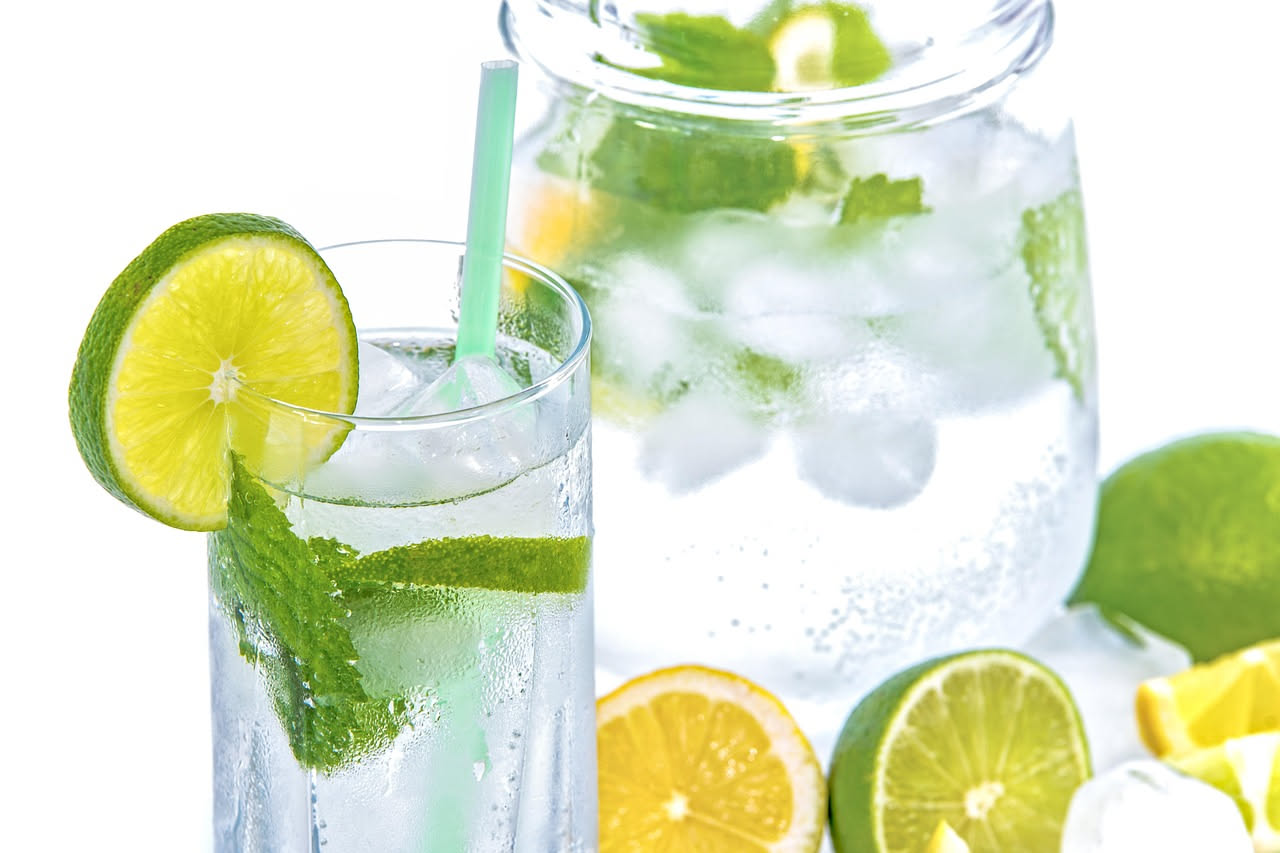 Bicchiere di acqua e limone con cubetti di ghiaccio e fette di limone su un tavolo di legno esposto al sole estivo, con gocce di condensa sul vetro
